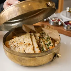 Fresh garlic naan bread garnished with herbs and served in a traditional brass container
