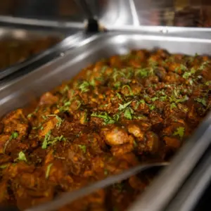 Indian chicken curry garnished with fresh cilantro and served in a stainless-steel catering tray